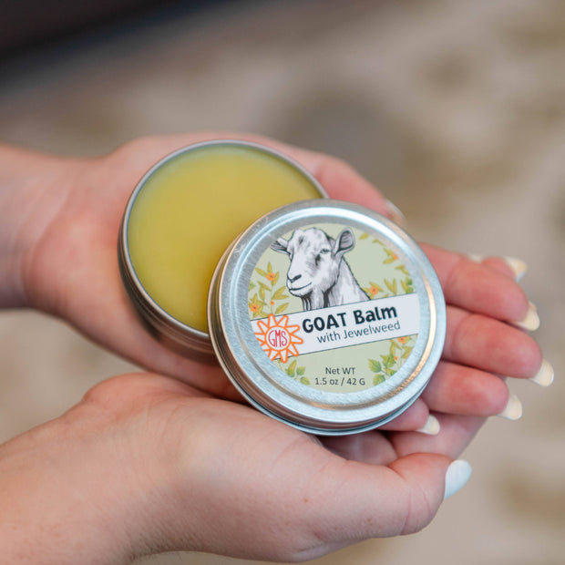 Person holding two tins of goat balm with a blurred background