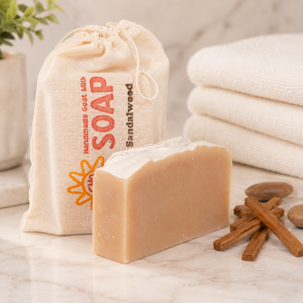 Bar of goat milk soap with a drawstring bag labeled 'Soap' and cinnamon sticks on a marble surface.