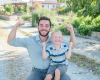Emery and Michael smiling and flexing their muscles while sitting together outdoors