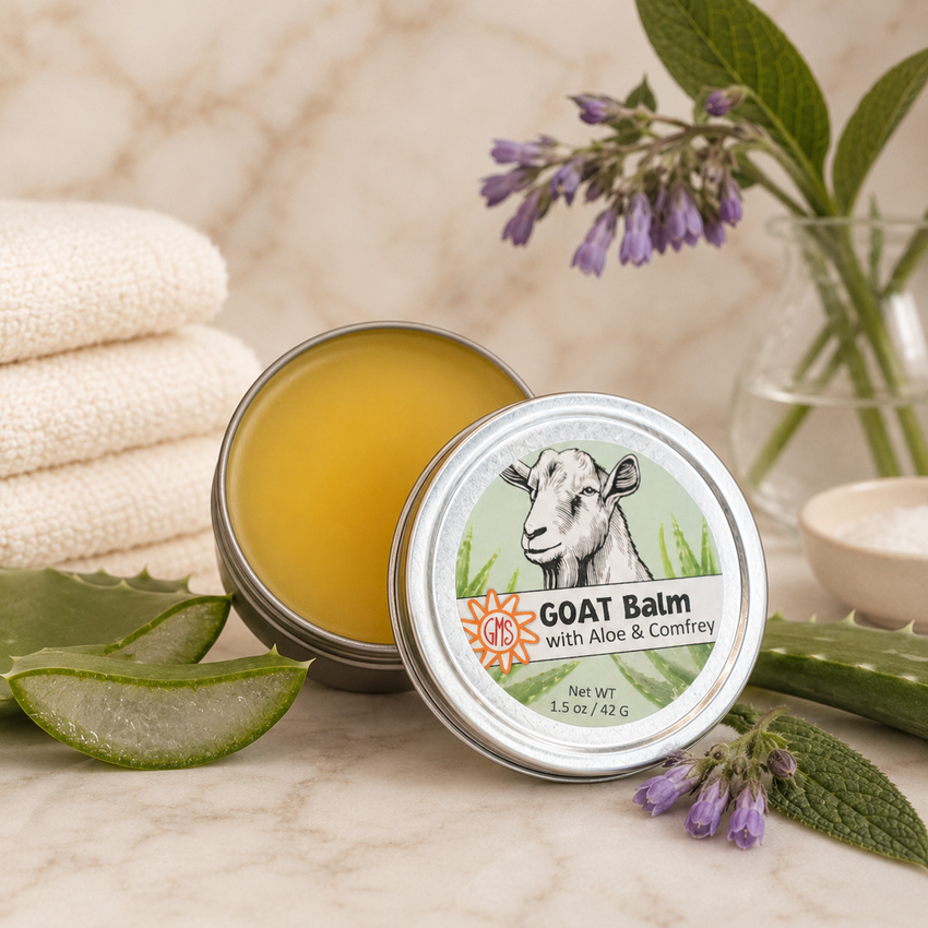 Goat balm tin with aloe and comfrey on a marble surface with towels and flowers.