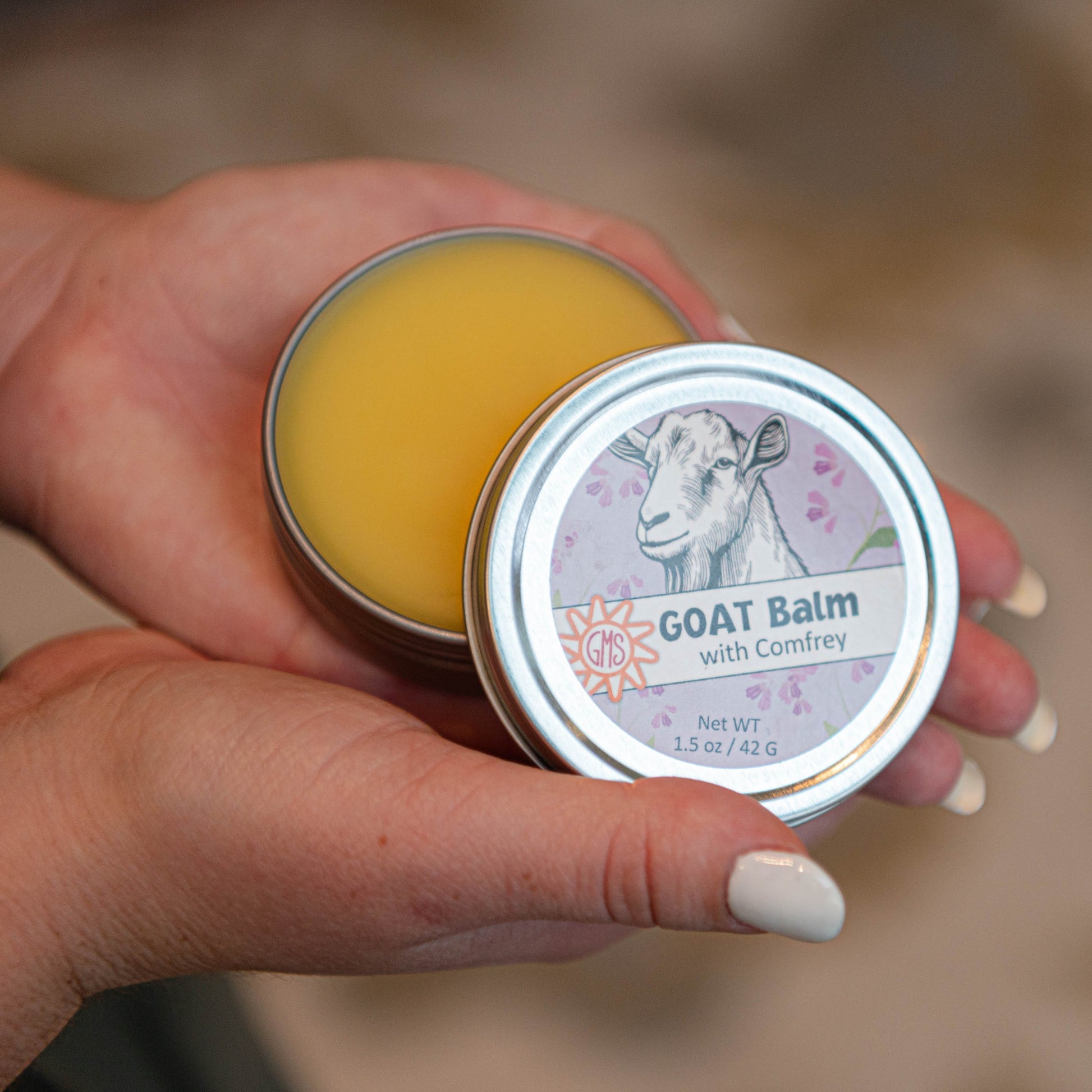 Hand holding a tin of Goat Balm with a blurred background