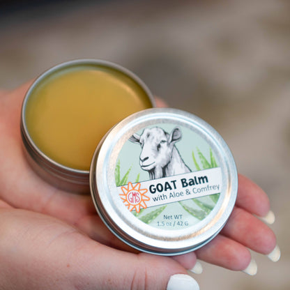 Hand holding a tin of goat balm with a blurred natural background