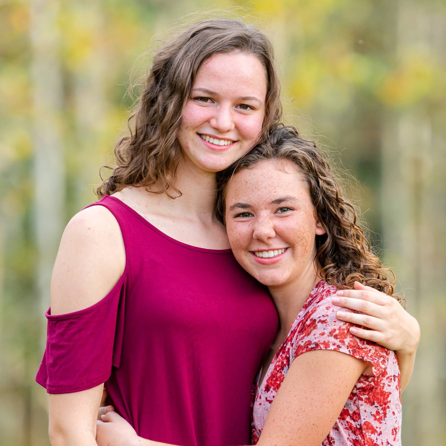Two women hugging in a forest with trees in the background