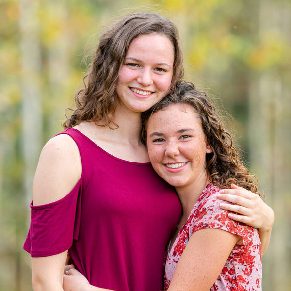 Two women hugging in a forest with trees in the background