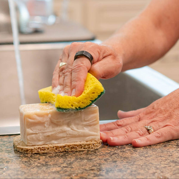 Person cleaning a kitchen countertop with a sponge and dish soap