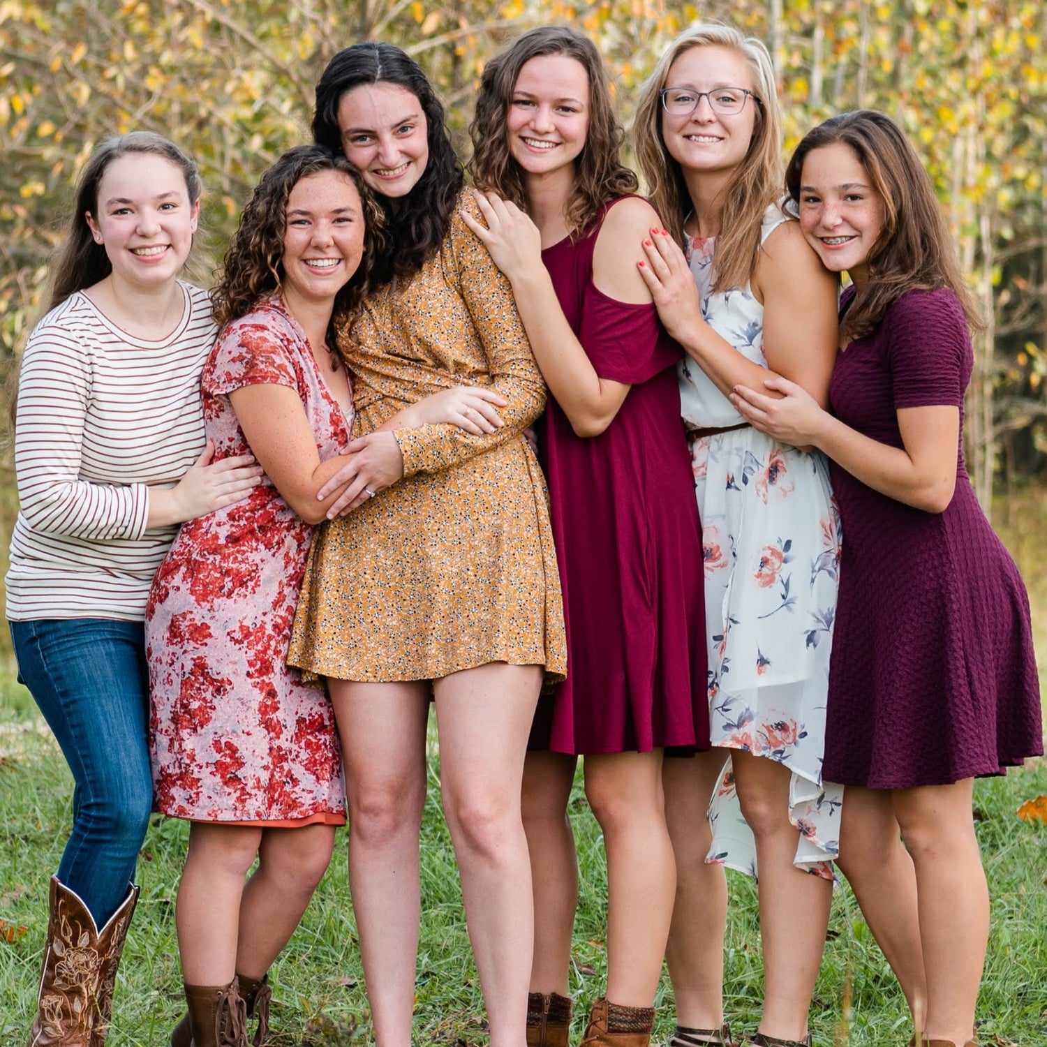 Five women posing together in a field with trees in the background