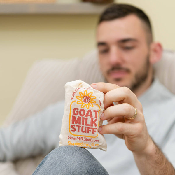 Man holding a bar of Goat Milk Stuff soap while sitting on a couch.