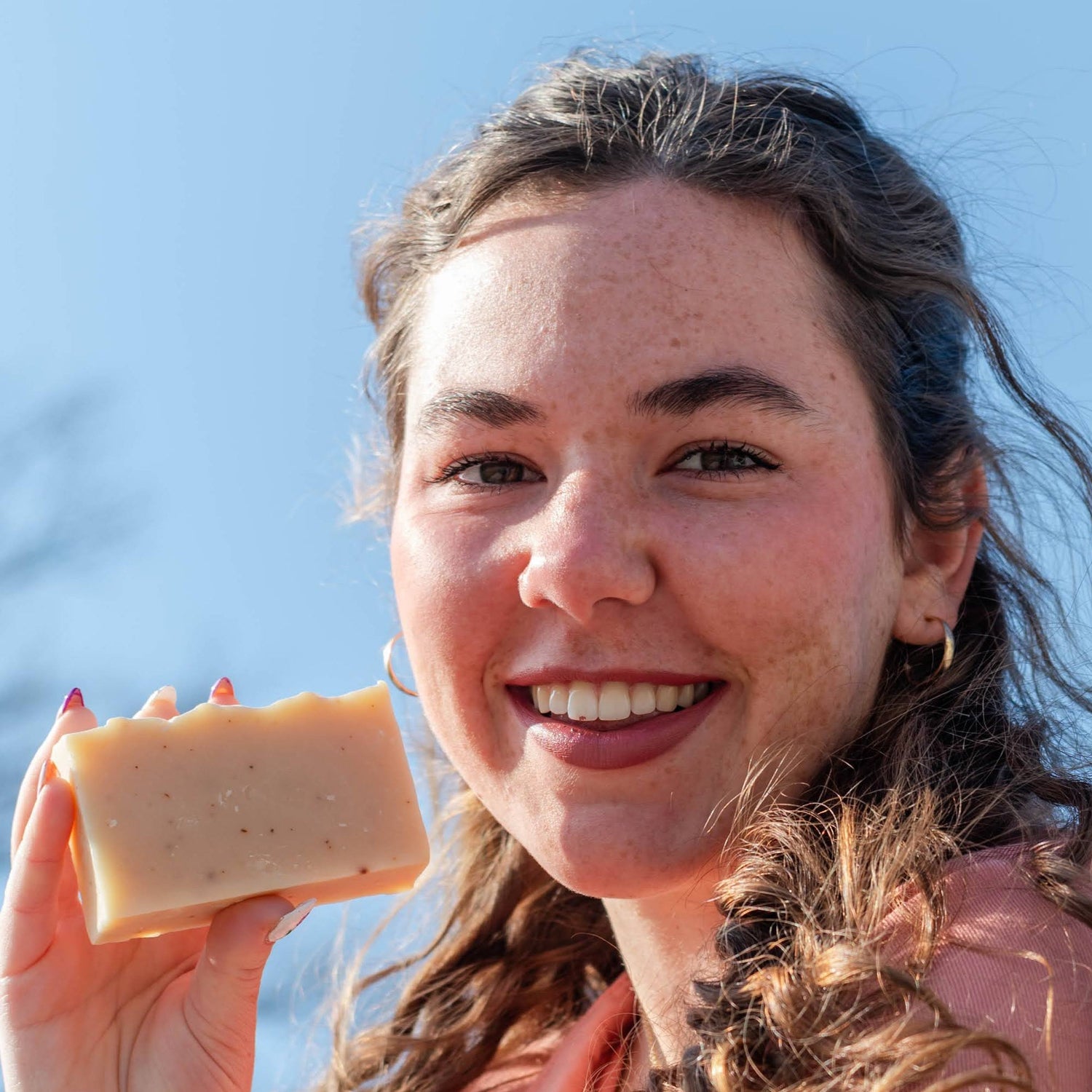 Woman holding a bar of soap outdoors with a clear blue sky.