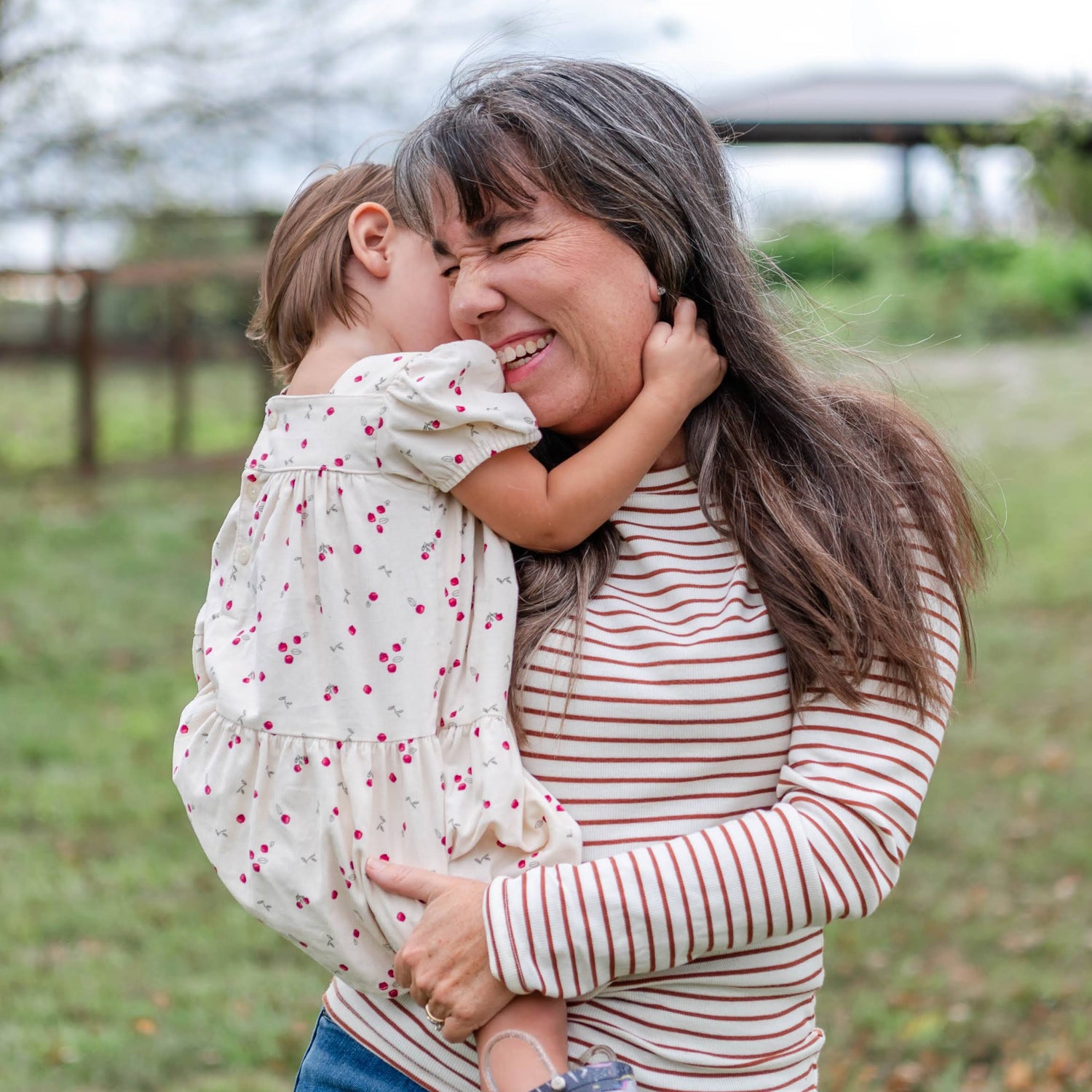 Grandma holding a child in an outdoor setting with trees and grass.