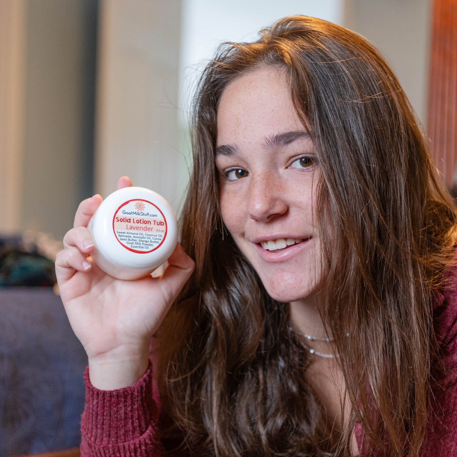 Woman holding a Goat Milk Stuff Lotion Tub, sitting on a couch.