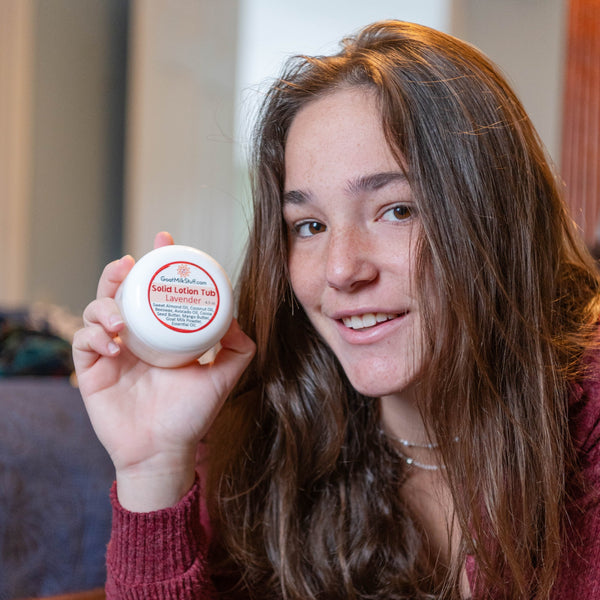 Woman holding a Goat Milk Stuff Lotion Tub, sitting on a couch.