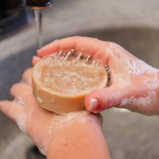 Hand holding a bar of luffa soap under running water