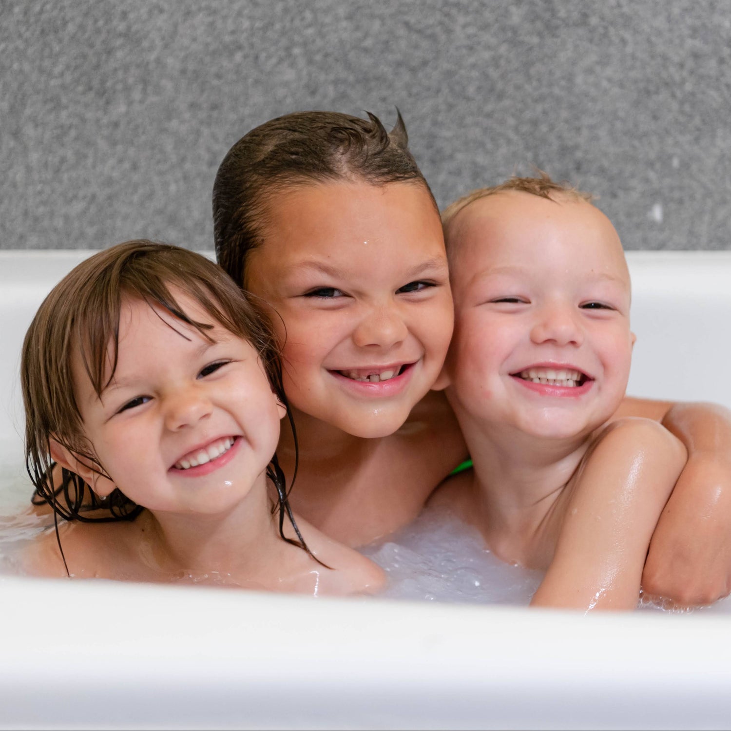 Three children in a bathtub, smiling with bubbles