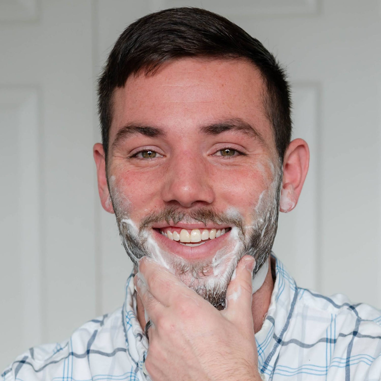 Man applying shaving soap to his face with a white background