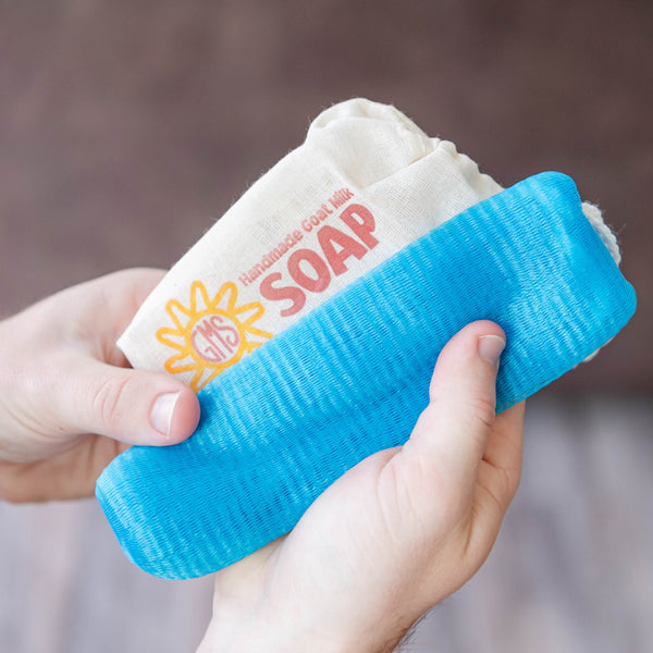 Hand holding a soap saver and a bar of Goat Milk Stuff soap