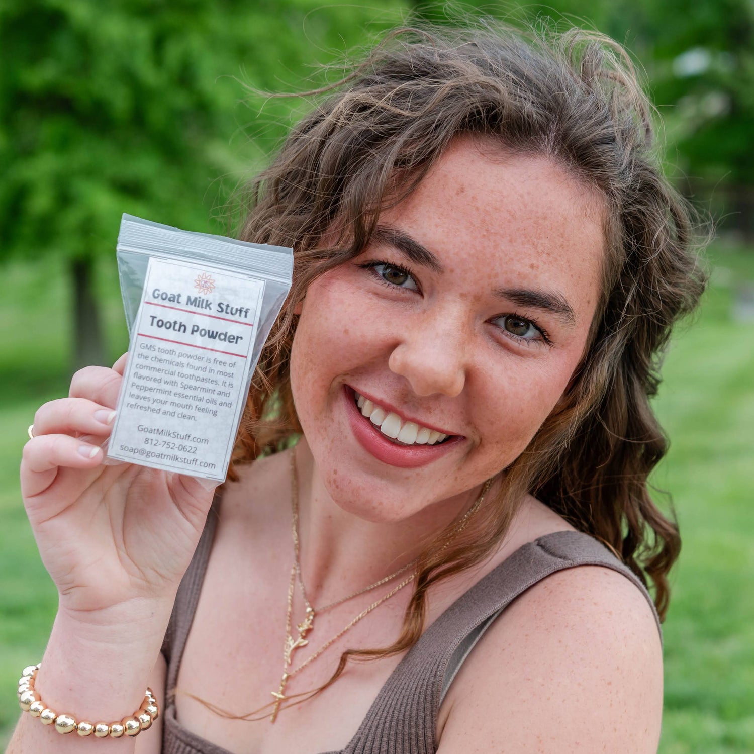 Woman holding Goat Milk Stuff's Tooth powder outdoors with greenery in the background