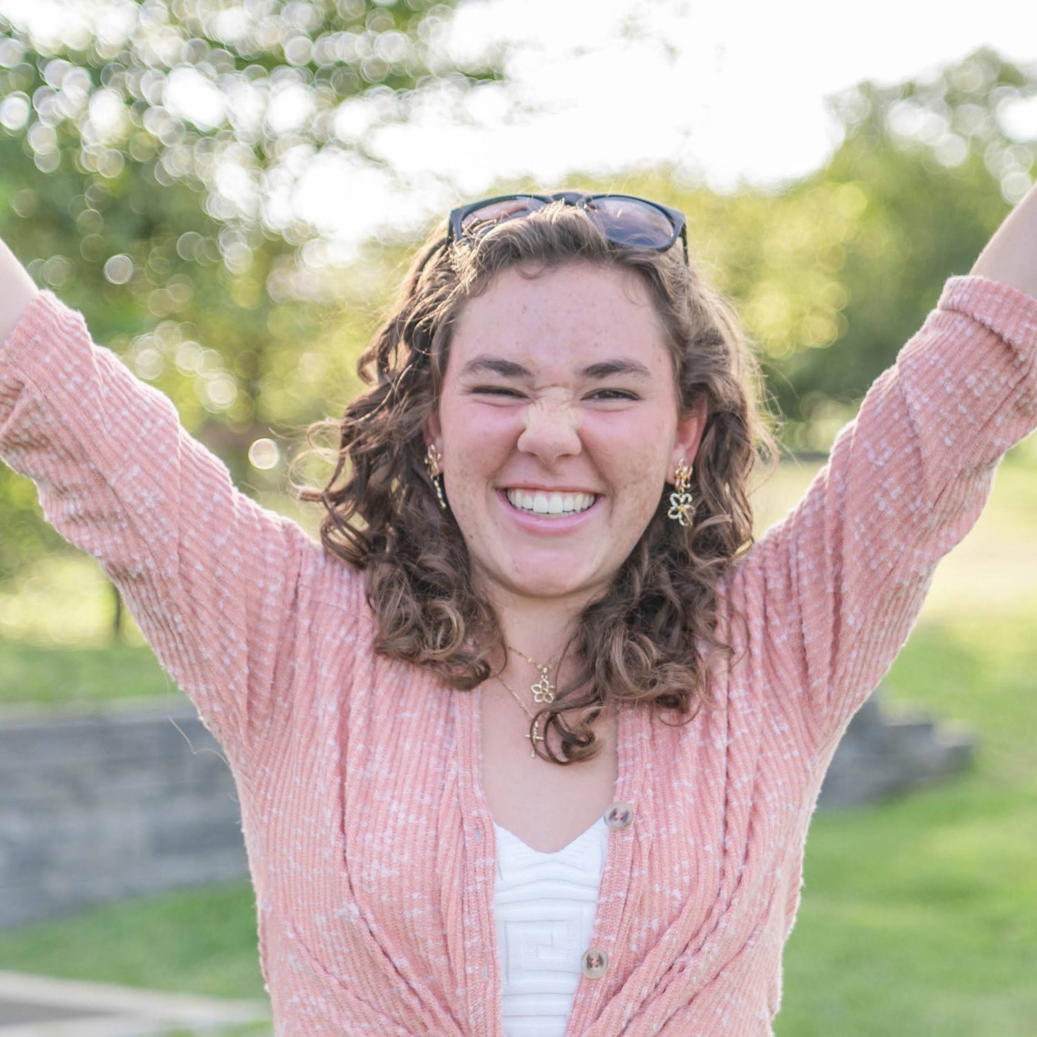 Woman in a pink cardigan with arms raised outdoors