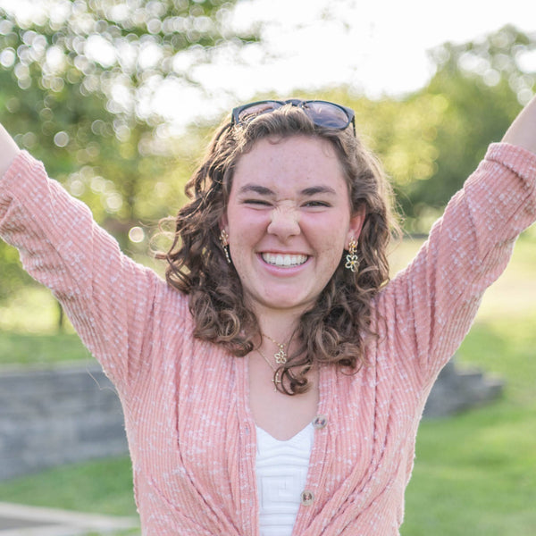 Woman in a pink cardigan with arms raised outdoors