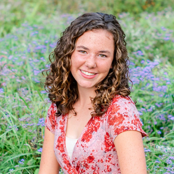 Woman in a red floral dress sitting in a field of flowers and grass.