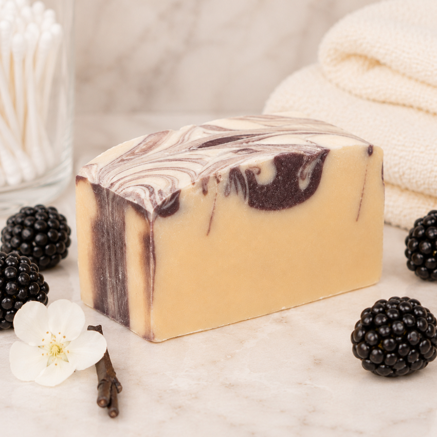 Bar of goat milk soap with blackberry and vanilla elements on a marble surface