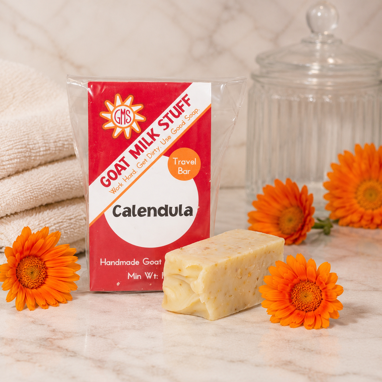Goat milk soap bar with packaging and calendula flowers on a marble surface