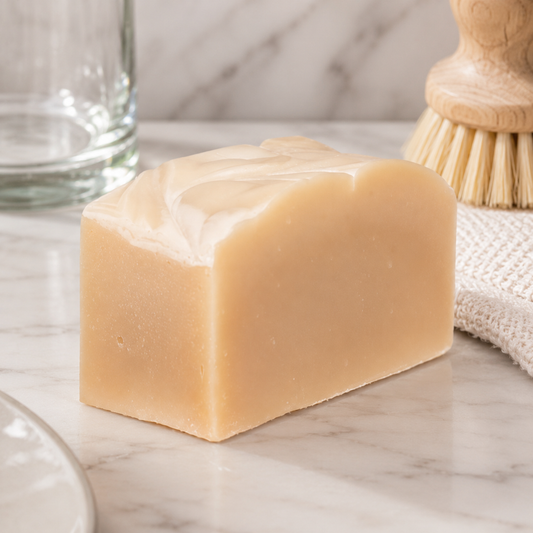 Bar of soap on a marble surface with a glass and wooden brush in the background