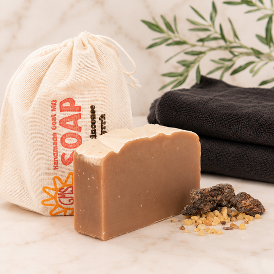 Bar of goat milk soap with a drawstring bag labeled 'Handmade Soap' and black towels in the background.