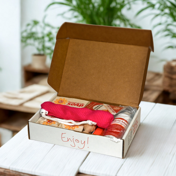 Open cardboard box with bath products on a wooden surface, plants in the background