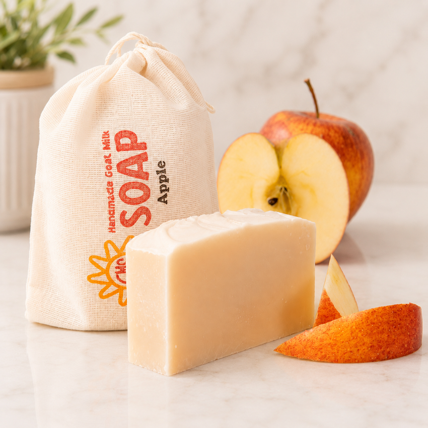 Bar of goat milk soap with an apple and a drawstring bag labeled 'Soap Apple' on a light surface.