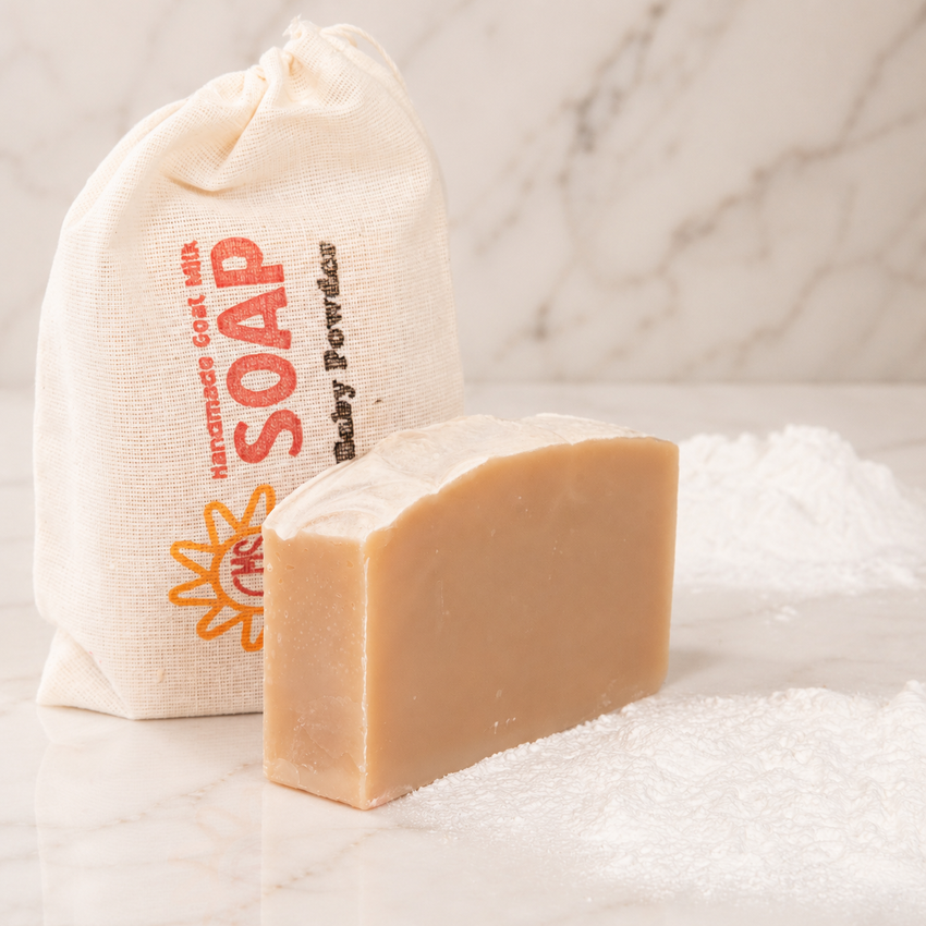 Bar of goat milk soap with a cloth bag labeled 'Soap' on a marble background