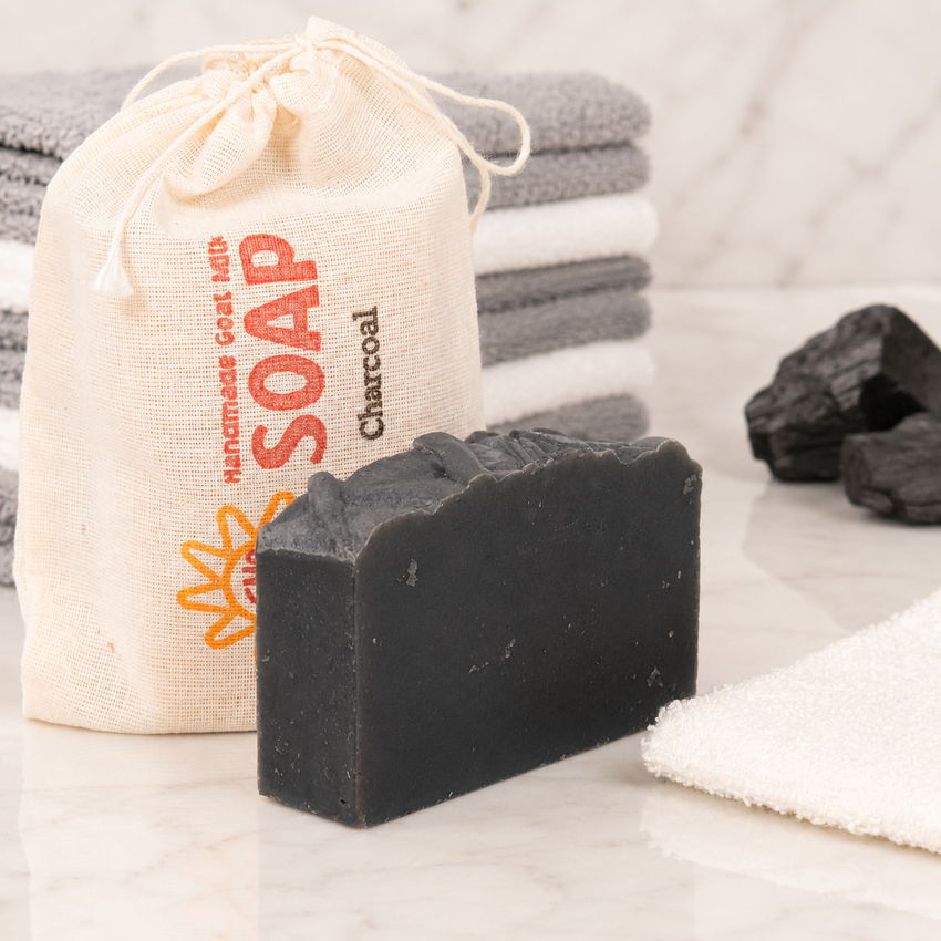 Bar of charcoal goat milk soap with a drawstring bag labeled 'Handmade Goat Milk Soap' on a marble surface.