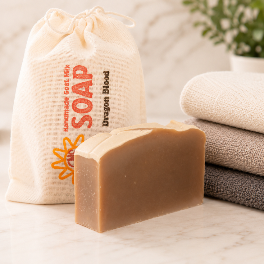 Bar of goat milk soap in front of a drawstring bag labeled 'Dragon Blood Soap' on a neutral background.