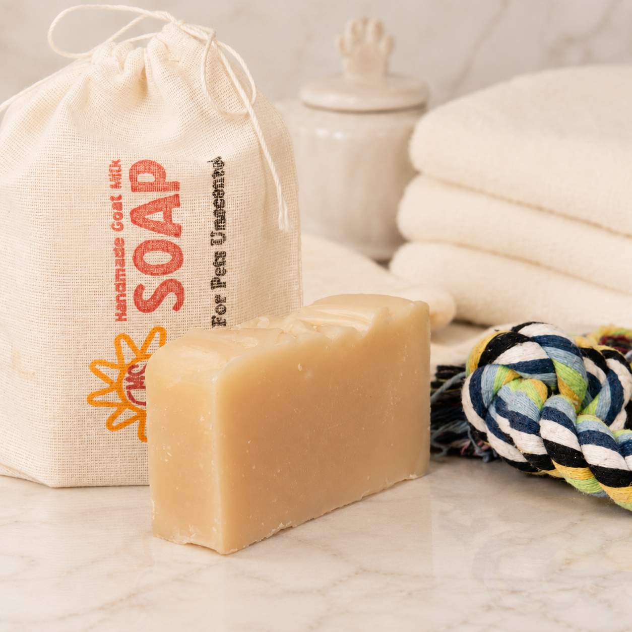 Bar of goat milk soap with a drawstring bag labeled 'Handmade Goat Milk Soap' and a rope toy in the background.