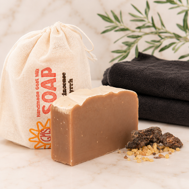 Bar of goat milk soap with a drawstring bag labeled 'Handmade Soap' and black towels in the background.