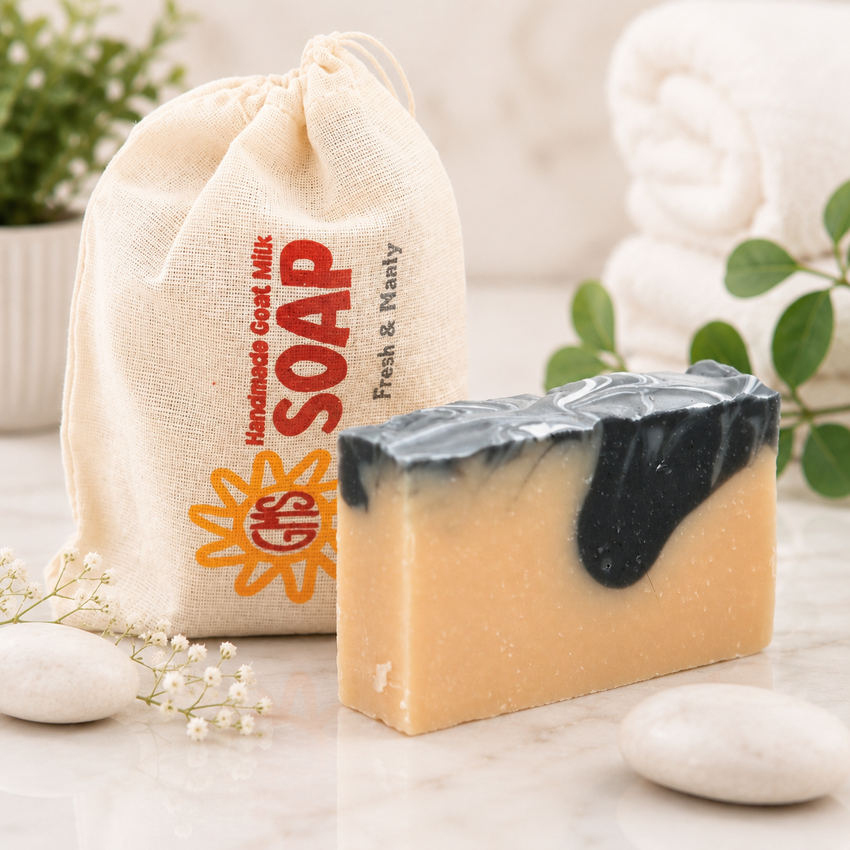 goat milk bar of soap with a black streak next to a drawstring bag labeled 'Handmade Goat Milk Soap' on a light surface.