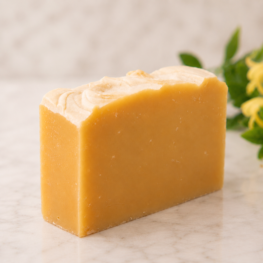 Bar of yellow goat milk soap on a marble surface with greenery in the background