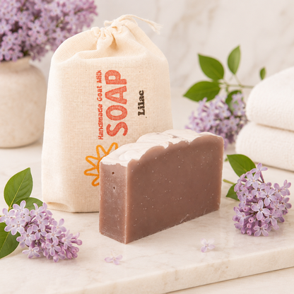 Bar of goat milk soap with a branded bag and lilac flowers on a marble surface