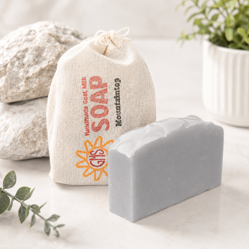 goat milk bar of soap with a drawstring bag labeled 'Mountaintop Soap' on a light surface.