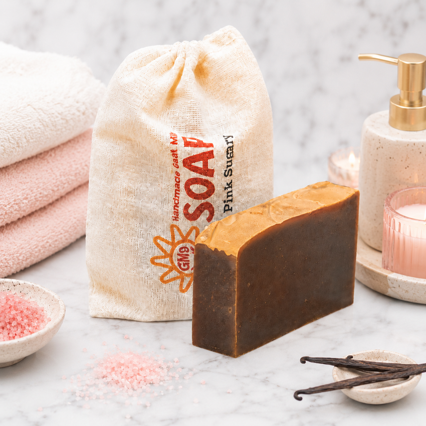 Bar of goat milk soap with a drawstring bag labeled 'SOAP' and a candle on a marble surface.