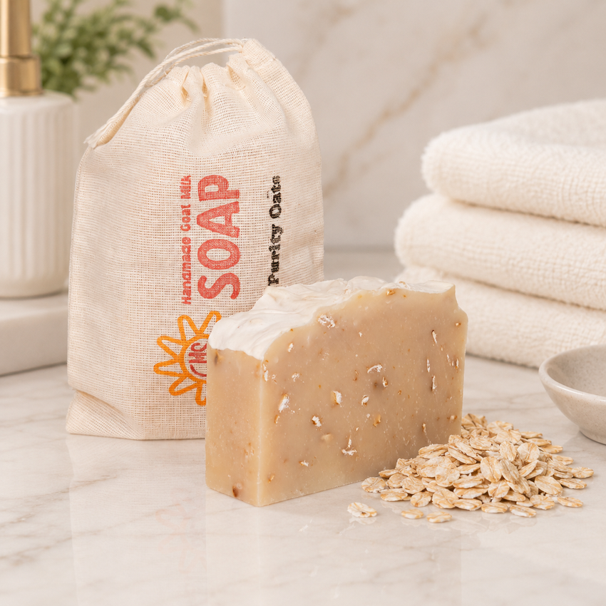 Bar of goat milk soap with oatmeal on a marble surface next to a drawstring bag labeled 'Soap' and folded towels.