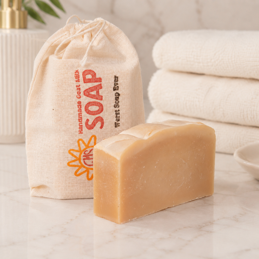 Bar of goat milk soap with a drawstring bag labeled 'SOAP' and towels in the background on a marble surface.