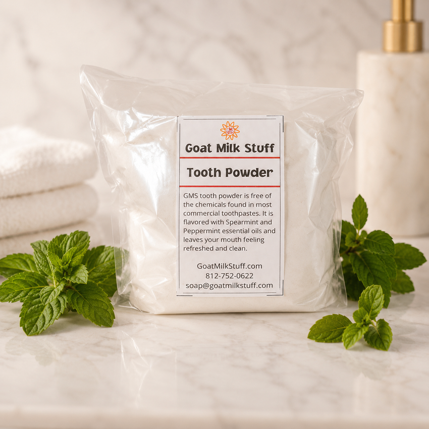 Packaged goat milk tooth powder with mint leaves on a bathroom counter