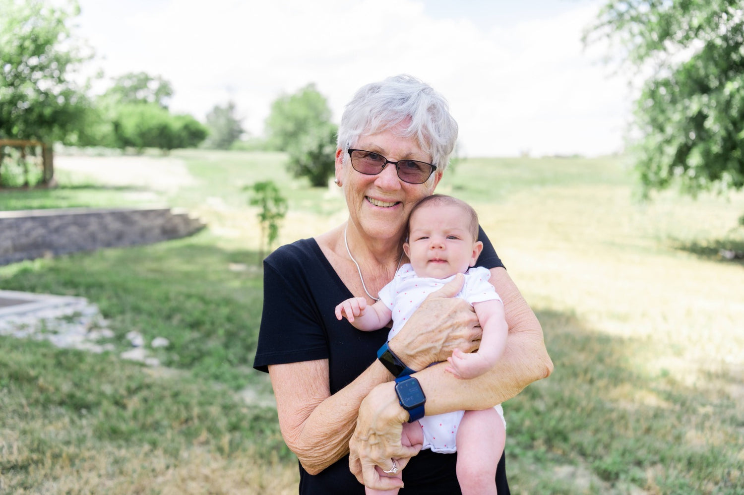 Grandma holding a baby outdoors in a park-like setting