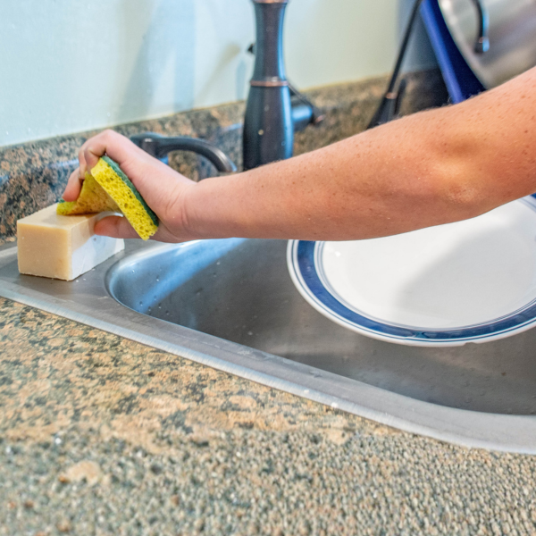 Person cleaning a kitchen sink with a sponge and soap bar.