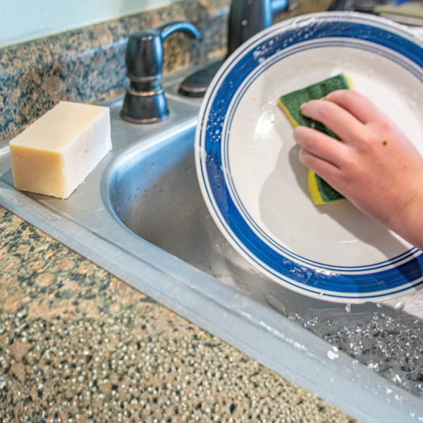 Person washing a plate with soap and water in a kitchen sink.