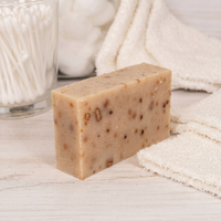 Bar of Persimmon soap on a wooden surface with a white towel and glass container in the background.