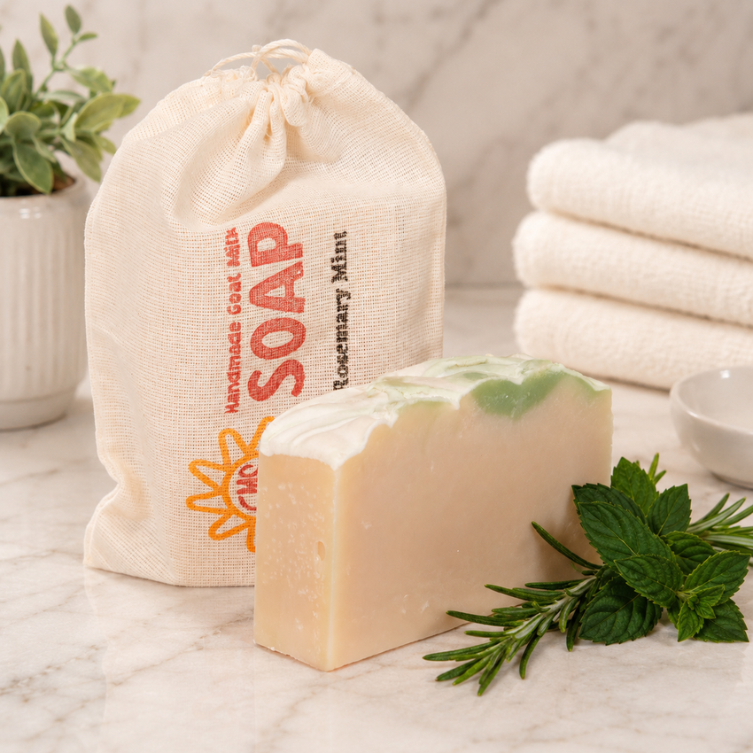 Bar of goat milk soap with a drawstring bag labeled 'Handmade Goat Milk Soap' and rosemary leaves on a marble surface.