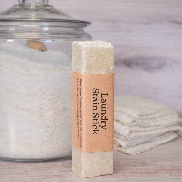 Laundry stain stick with a label in front of a glass jar and folded towels.