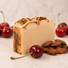 Bar of goat milk soap with dotted surface, cherries, and almonds on a light background