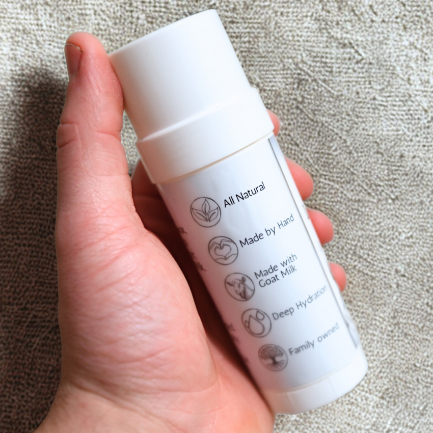 Hand holding a white skincare product container with text on a textured surface